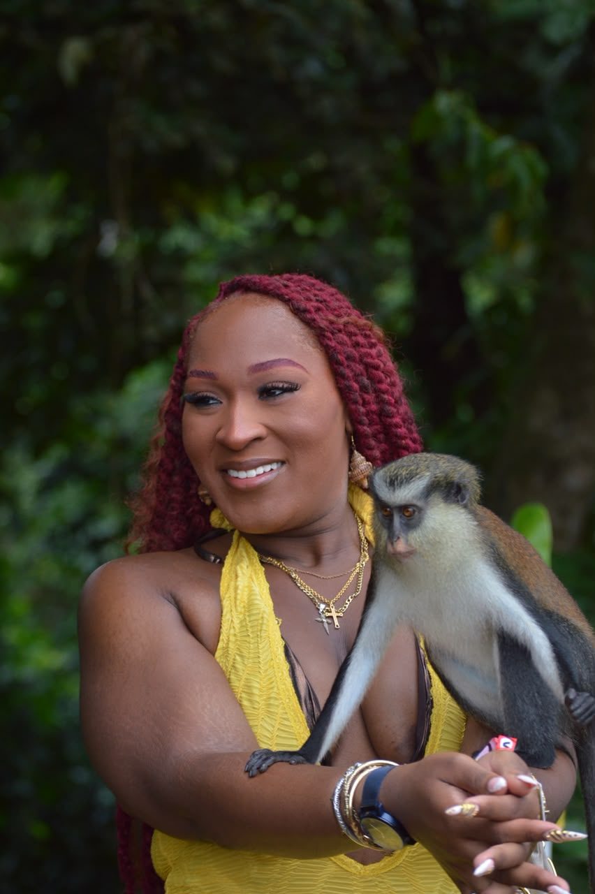 A guest laughing as a mona monkey sits on her arm